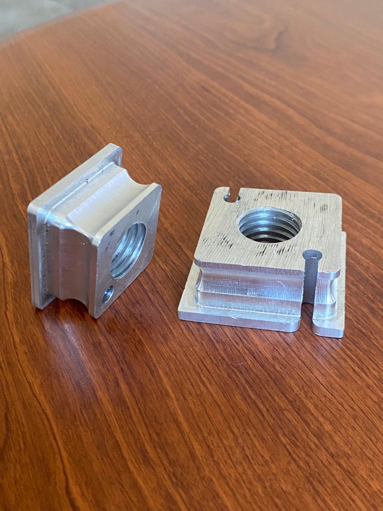Two CNC machined aluminum rectangular T-slot nut blocks with threaded center holes and side slots